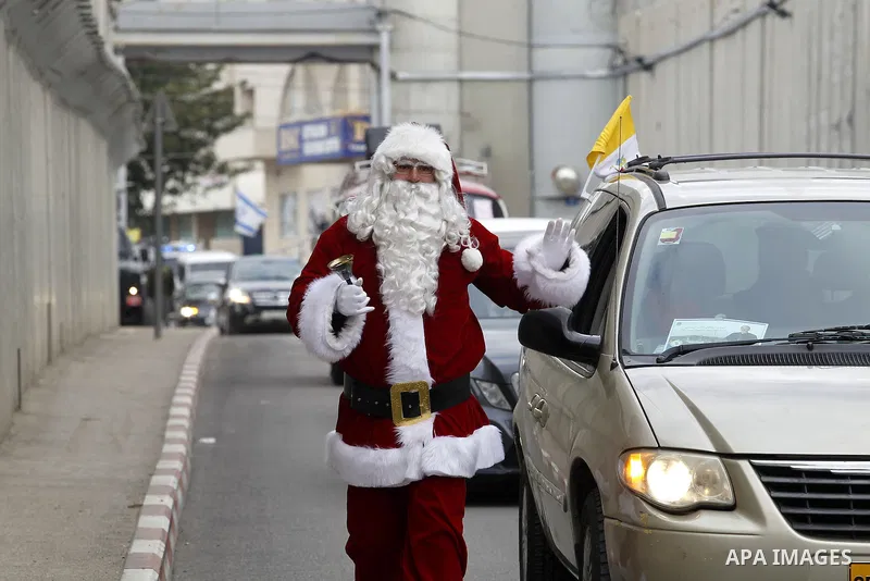 A Palestinian dressed as Santa Claus gestures as the Latin Patriarch of Jerusalem Pierbattista Pizzaballa arrives through an Israeli checkpoint to attend Christmas celebrations, in the city of Bethlehem in the Israeli-oc...