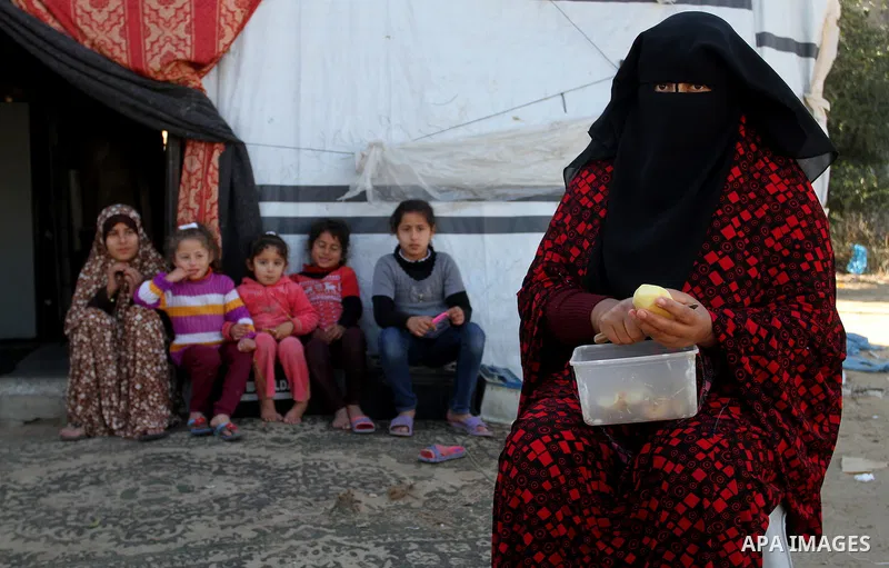 A Palestinian woman from Abu Jamea family cooks outside her house which was destroyed during the 50-day war between Israel and Hamas militants in the summer of 2014, on in Khan Younis in the southern Gaza Strip December...