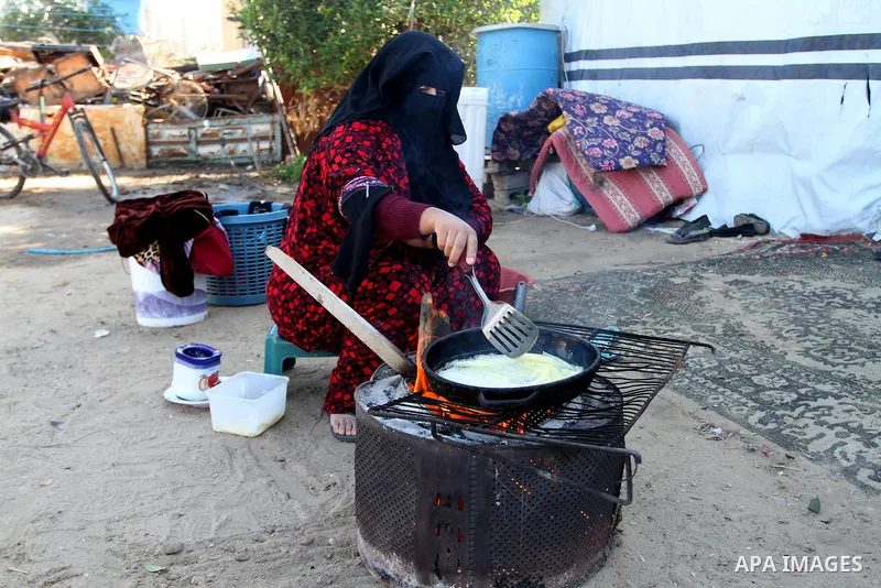 A Palestinian woman from Abu Jamea family cooks outside her house which was destroyed during the 50-day war between Israel and Hamas militants in the summer of 2014, on in Khan Younis in the southern Gaza Strip December...