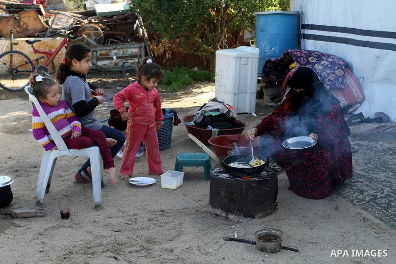 A Palestinian woman from Abu Jamea family cooks outside her house which was destroyed during the 50-day war between Israel and Hamas militants in the summer of 2014, on in Khan Younis in the southern Gaza Strip December...