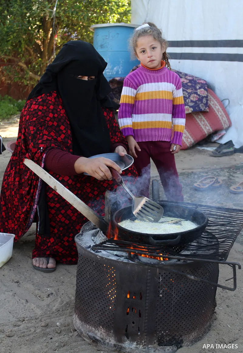 A Palestinian woman from Abu Jamea family cooks outside her house which was destroyed during the 50-day war between Israel and Hamas militants in the summer of 2014, on in Khan Younis in the southern Gaza Strip December...