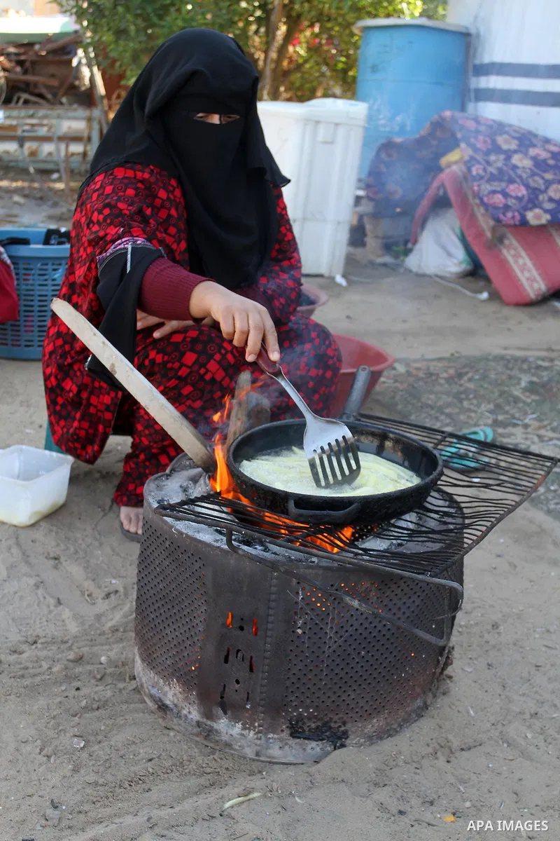 A Palestinian woman from Abu Jamea family cooks outside her house which was destroyed during the 50-day war between Israel and Hamas militants in the summer of 2014, on in Khan Younis in the southern Gaza Strip December...