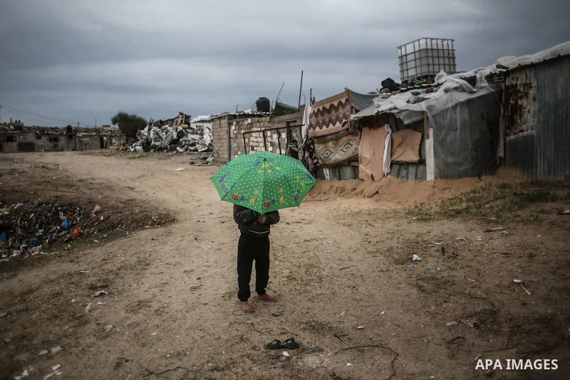 A barefoot Palestinian boy holds an umbrella as he plays during rainy, cold weather in a slum on the outskirts of Khan Younis refugee camp, southern Gaza Strip, on December 28, 2016. Photo by Mohammed Dahman