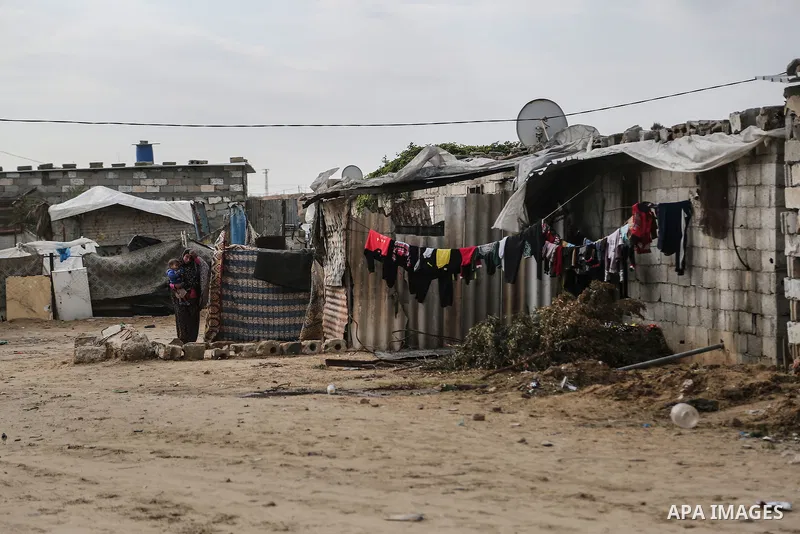 A Palestinian woman carries her child during rainy, cold weather outside her house in a slum on the outskirts of Khan Younis refugee camp, southern Gaza Strip, on December 28, 2016. Photo by Mohammed Dahman