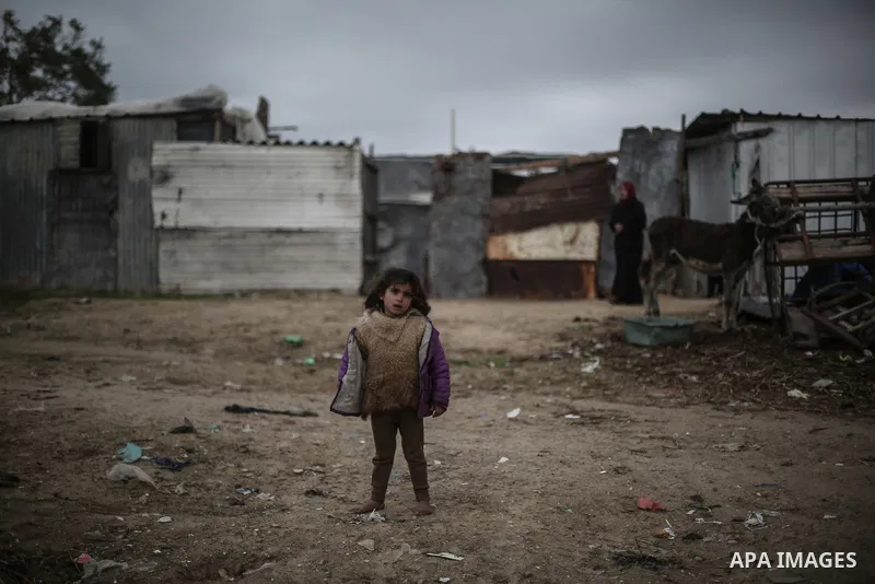 A barefoot Palestinian girl poses for a photo during rainy, cold weather outside her family house in a slum on the outskirts of Khan Younis refugee camp, southern Gaza Strip, on December 28, 2016. Photo by Mohammed Dahma...