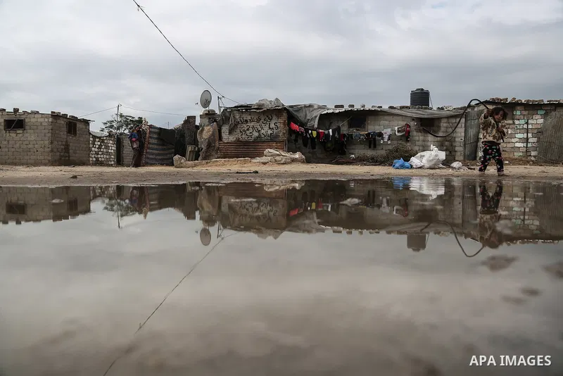 A barefoot Palestinian girl is reflected in a puddle while playing in rainy, cold weather next to her family house in a slum on the outskirts of Khan Younis refugee camp, southern Gaza Strip, on December 28, 2016. Photo...