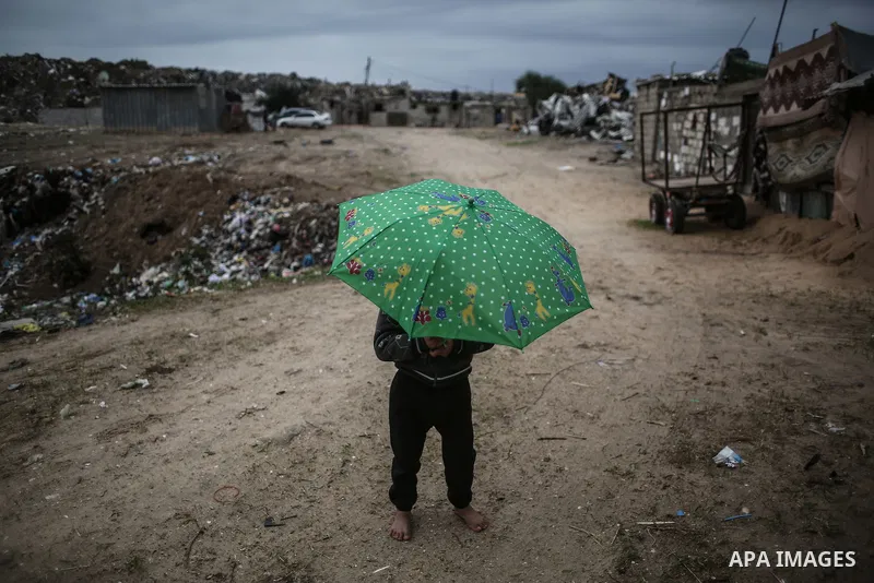 A barefoot Palestinian boy holds an umbrella as he plays during rainy, cold weather in a slum on the outskirts of Khan Younis refugee camp, southern Gaza Strip, on December 28, 2016. Photo by Mohammed Dahman