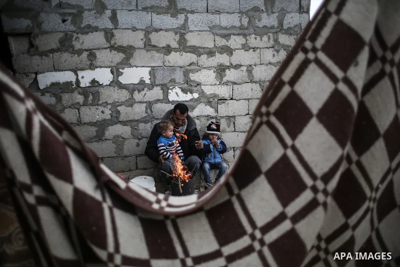 A Palestinian man and his children warm themselves around the fire during rainy, cold weather outside their house in a slum on the outskirts of Khan Younis refugee camp, southern Gaza Strip, on December 28, 2016. Photo b...