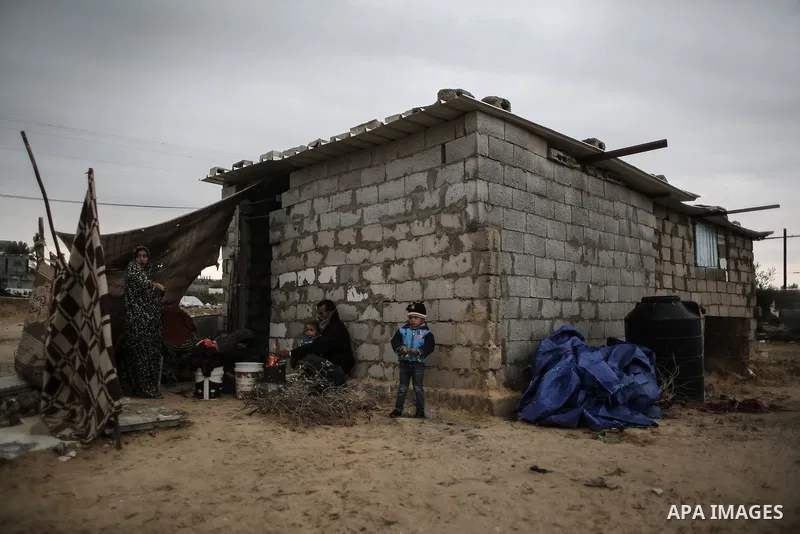 A Palestinian man and his family warm themselves around the fire during rainy, cold weather outside their house in a slum on the outskirts of Khan Younis refugee camp, southern Gaza Strip, on December 28, 2016. Photo by...