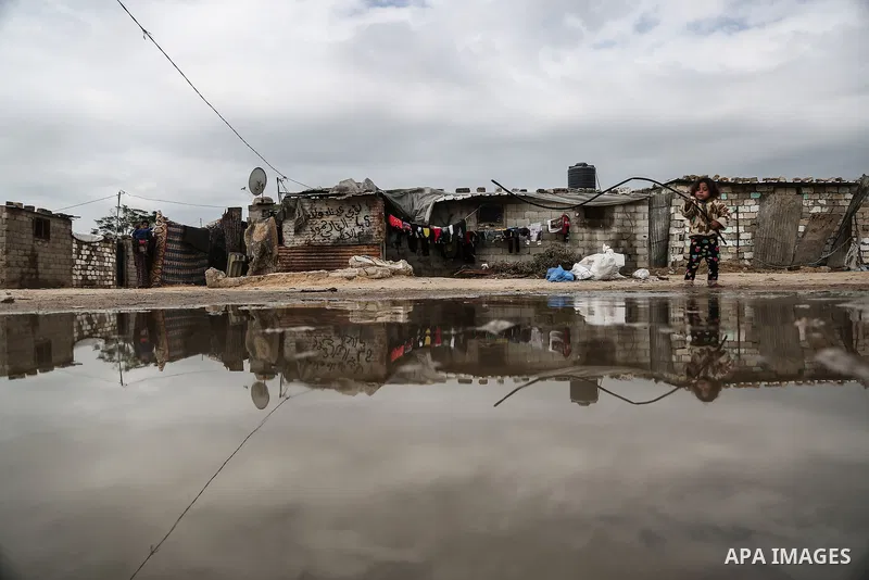 A barefoot Palestinian girl is reflected in a puddle while playing in rainy, cold weather next to her family house in a slum on the outskirts of Khan Younis refugee camp, southern Gaza Strip, on December 28, 2016. Photo...
