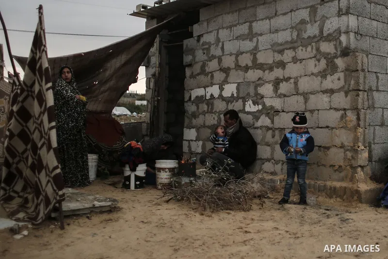 A Palestinian man and his children warm themselves around the fire during rainy, cold weather outside their house in a slum on the outskirts of Khan Younis refugee camp, southern Gaza Strip, on December 28, 2016. Photo b...