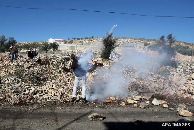 A Palestinian protester throws back a tear gas canisters towards Israeli security forces during clashes following a demonstration against the expropriation of Palestinian land by Israel in the village of Kfar Qaddum, nea...