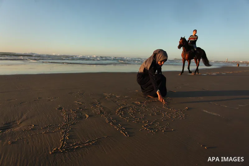 A Palestinian girl writes on a sand read "2017" during the last sunset of 2016 on the beach of Gaza City, on December 31, 2016. Photo by Ashraf Amra