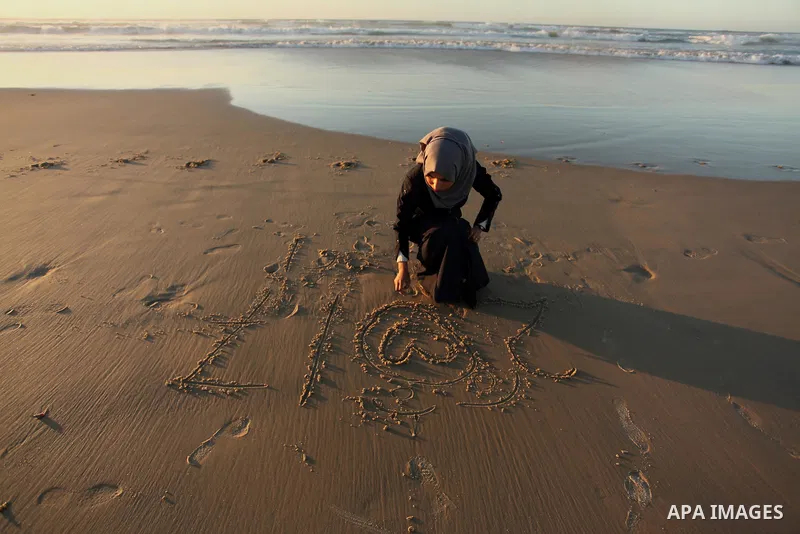 A Palestinian girl writes on a sand read "2017" during the last sunset of 2016 on the beach of Gaza City, on December 31, 2016. Photo by Ashraf Amra