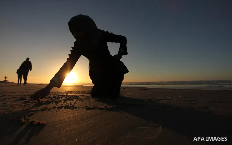 A Palestinian girl writes on a sand read "2017" during the last sunset of 2016 on the beach of Gaza City, on December 31, 2016. Photo by Ashraf Amra