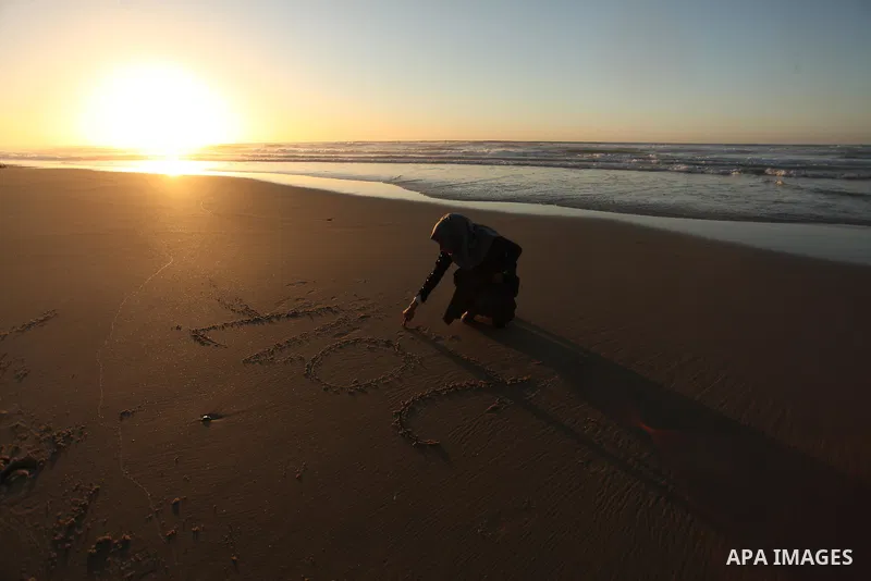 A Palestinian girl writes on a sand read "2017" during the last sunset of 2016 on the beach of Gaza City, on December 31, 2016. Photo by Ashraf Amra