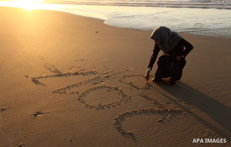 A Palestinian girl writes on a sand read "2017" during the last sunset of 2016 on the beach of Gaza City, on December 31, 2016. Photo by Ashraf Amra