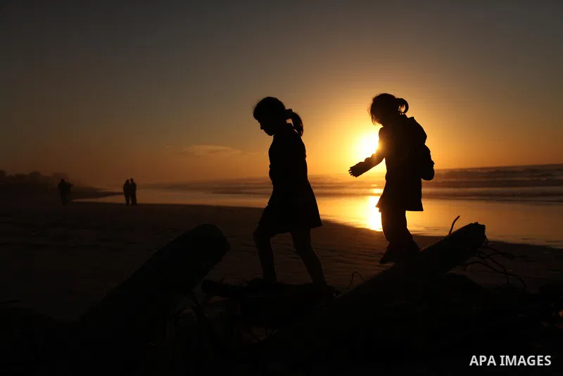 Palestinians walk on the beach of Gaza City, during the last sunset of 2016, on December 31, 2016. Photo by Ashraf Amra