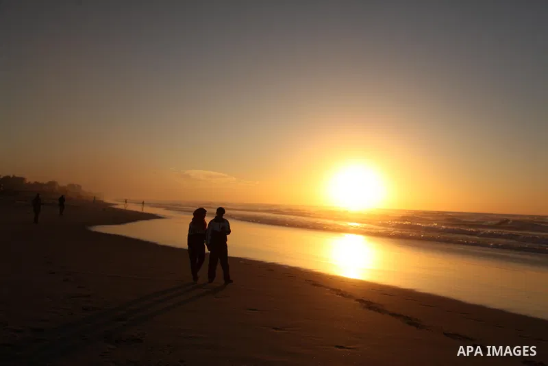 Palestinians walk on the beach of Gaza City, during the last sunset of 2016, on December 31, 2016. Photo by Ashraf Amra