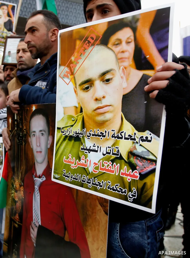 A Palestinian holds a poster of Israeli Sergeant Elor Azaria that reads "wanted" who killed the Palestinian Abdel Fattah al-Sharif during a protest in the West Bank city of Hebron on January 4, 2017. Photo by Wisam Hashl...