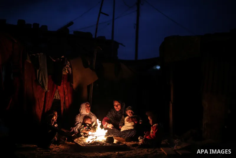 A picture taken on January 5, 2017 shows Palestinian family warm themselves around the fire outside their dwellings during the power cut on winter season in Khan Younis, in the southern Gaza strip. Photo by Mohammed Dahm...