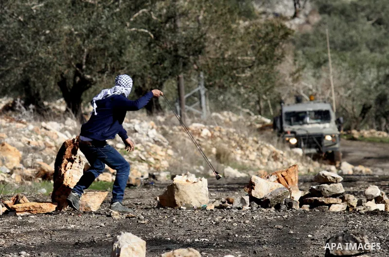 A Palestinian protester uses aslingshot to hurl stones towards Israeli security forces during clashes following a demonstration against the expropriation of Palestinian land by Israel in the village of Kfar Qaddum, near...