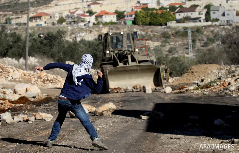 A Palestinian protester hurls stones towards a digger operated by Israeli security forces during clashes following a demonstration against the expropriation of Palestinian land by Israel in the village of Kfar Qaddum, ne...