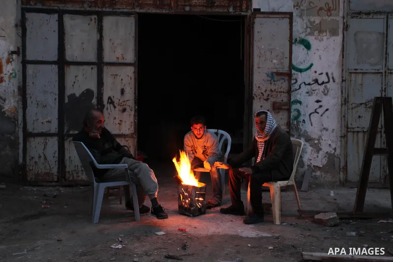 Palestinian family warm themselves around the fire outside their dwellings during the power cut on winter season in Shati refugee camp on 14 January 2017. Photo by Ashraf Amra
