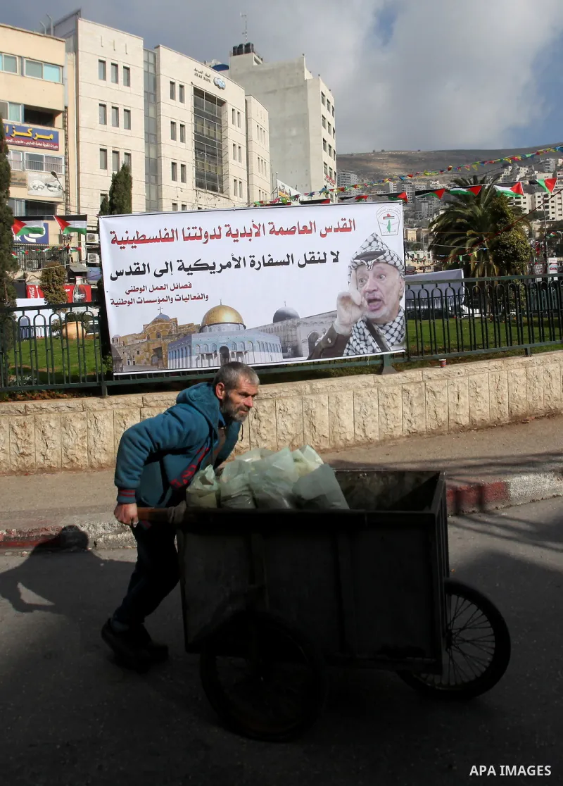 A Palestinian vendor passes by a banner bearing a portrait of late Palestinian leader Yasser Arafat against a promise by U.S. President-elect Donald Trump to relocate the U.S. embassy to Jerusalem, in the West Bank city...