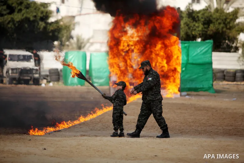 A Palestinian man helps a boy set fire to an Israeli flag during a military graduation ceremony for Palestinian National Security Forces loyal to Hamas in Gaza City January 22, 2017. Photo by Ashraf Amra