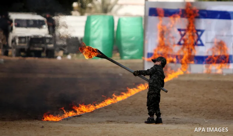 A Palestinian boy sets fire to a line of flames leading to an Israeli flag during a military graduation ceremony for Palestinian National Security Forces loyal to Hamas in Gaza City January 22, 2017. Photo by Ashraf Amra