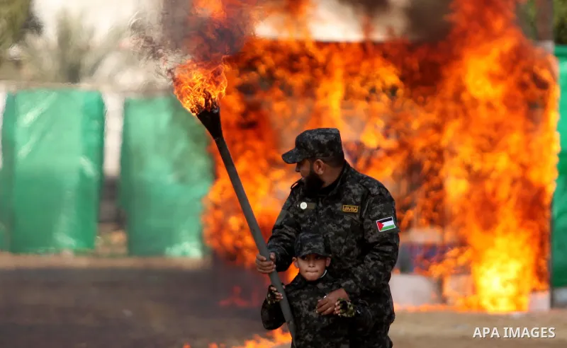 A Palestinian man helps a boy set fire to an Israeli flag during a military graduation ceremony for Palestinian National Security Forces loyal to Hamas in Gaza City January 22, 2017. Photo by Ashraf Amra