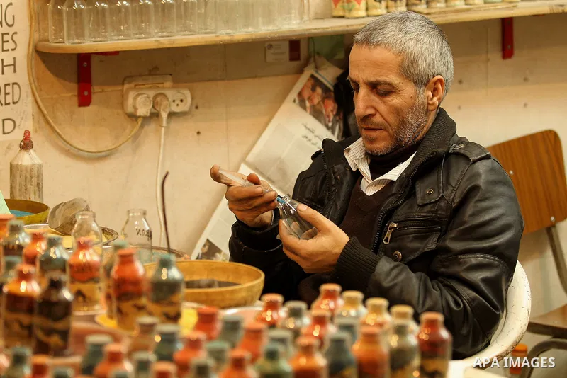 A Palestinian man paints on glass pots using colored sand, at his work shop in the Old City of the West Bank town of Hebron, on January 25, 2017. Photo by Wisam Hashlamoun