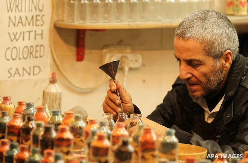 A Palestinian man paints on glass pots using colored sand, at his work shop in the Old City of the West Bank town of Hebron, on January 25, 2017. Photo by Wisam Hashlamoun