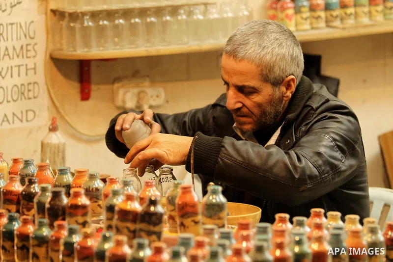 A Palestinian man paints on glass pots using colored sand, at his work shop in the Old City of the West Bank town of Hebron, on January 25, 2017. Photo by Wisam Hashlamoun