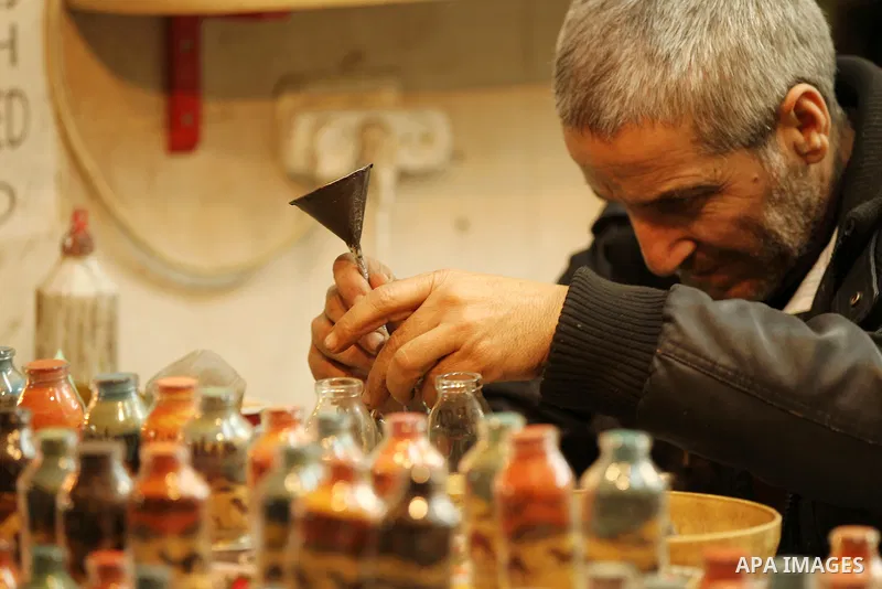 A Palestinian man paints on glass pots using colored sand, at his work shop in the Old City of the West Bank town of Hebron, on January 25, 2017. Photo by Wisam Hashlamoun