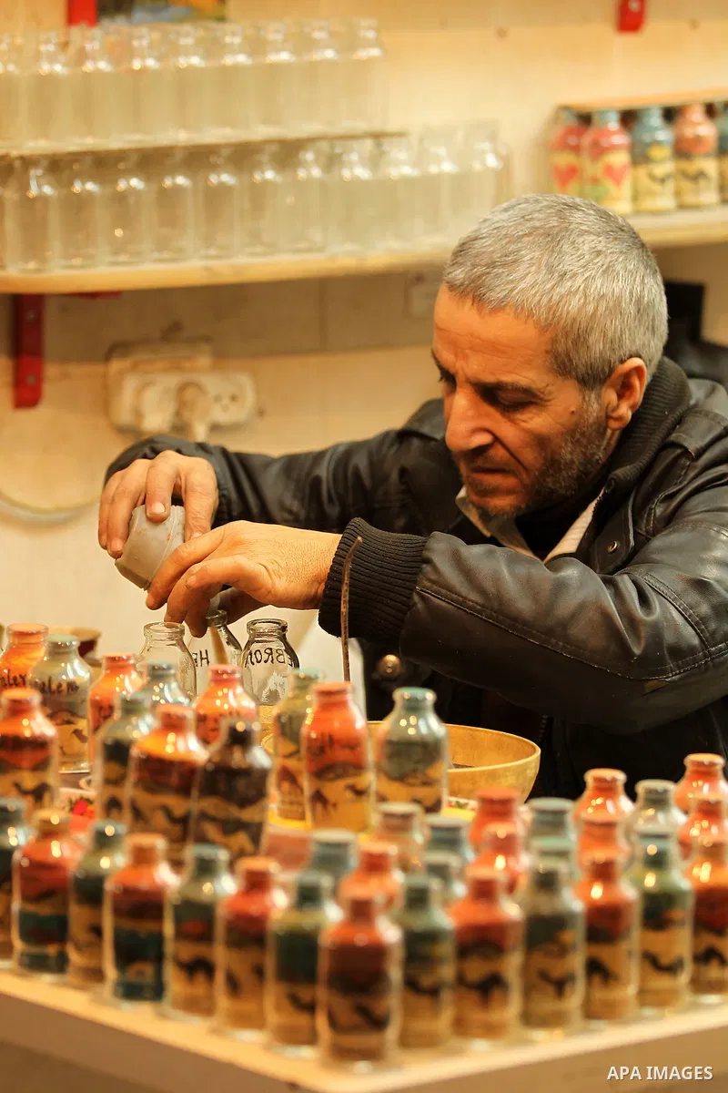 A Palestinian man paints on glass pots using colored sand, at his work shop in the Old City of the West Bank town of Hebron, on January 25, 2017. Photo by Wisam Hashlamoun