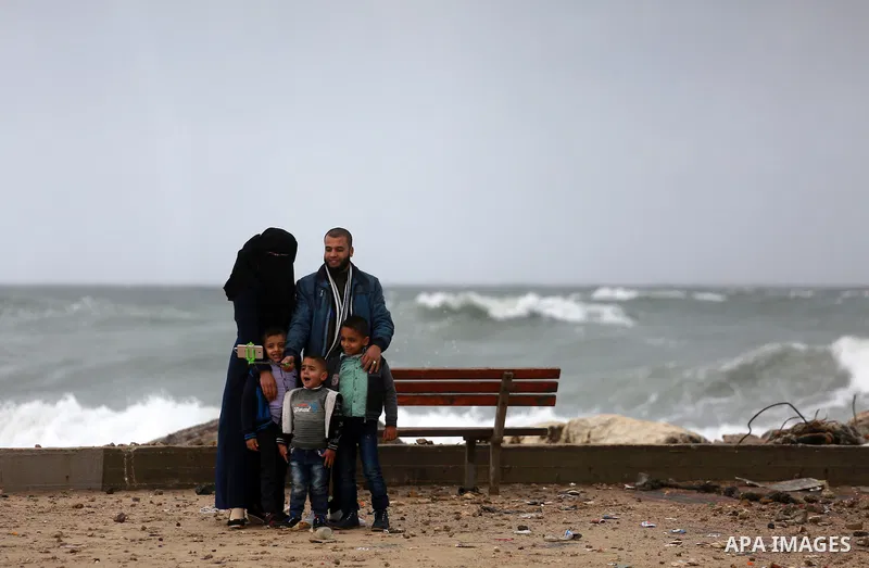 A Palestinian man and his family poses for a photo at the Gaza seaport during a rainy and heavy wind weather prevails on the Mediterranean Sea, in Gaza City on January 28, 2017. Photo by Mohammed Asad
