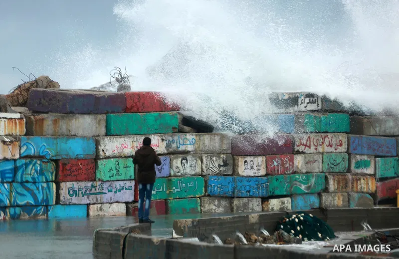 A Palestinian man stands on wall as a huge wave crash over a sea wall at the Gaza seaport during a rainy and heavy wind weather prevails on the Mediterranean Sea, in Gaza City on January 28, 2017. Photo by Mohammed Asad