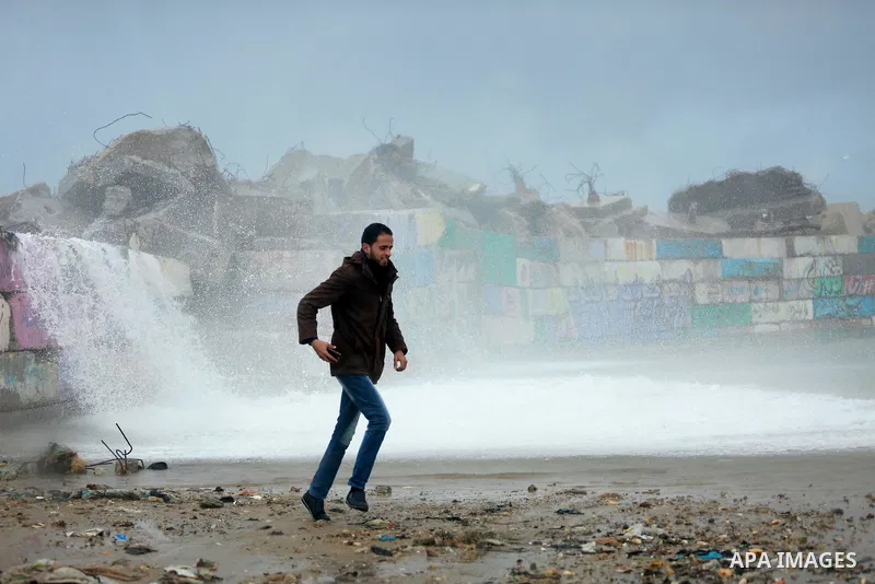 A Palestinian man runs as a huge wave crash over a sea wall at the Gaza seaport during a rainy and heavy wind weather prevails on the Mediterranean Sea, in Gaza City on January 28, 2017. Photo by Mohammed Asad