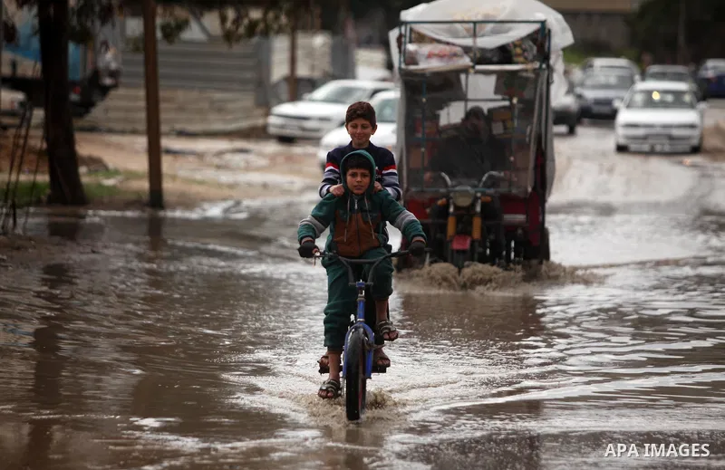 Two Palestinian boys ride a bicycle through a wet street during the cold and rainy weather in the Jabalia refugee camp in the northern Gaza Strip on January 28, 2017. Photo by Ashraf Amra