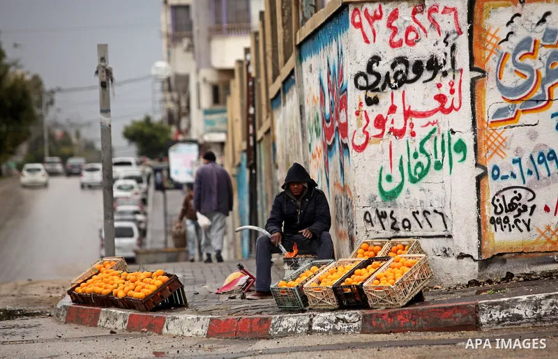 A Palestinian fruit-seller lights a fire to warm up during the cold and rainy weather in Gaza city on January 28, 2017. Photo by Ashraf Amra