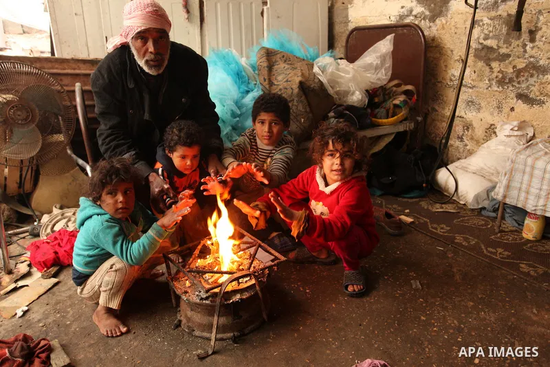 Palestinian children warm up in front of a fire in a hovel during the cold and rainy weather in the Jabalia refugee camp in the northern Gaza Strip on January 28, 2017. Photo by Ashraf Amra