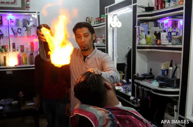 Ramadan Edwan, a Palestinian barber, uses fire in a hair-straightening technique with a client at his salon in the Rafah refugee camp, in the southern Gaza Strip on February 2, 2017. Photo by Abed Rahim Khatib
