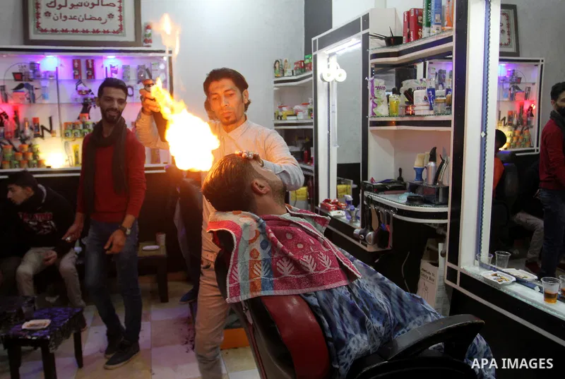 Ramadan Edwan, a Palestinian barber, uses fire in a hair-straightening technique with a client at his salon in the Rafah refugee camp, in the southern Gaza Strip on February 2, 2017. Photo by Abed Rahim Khatib