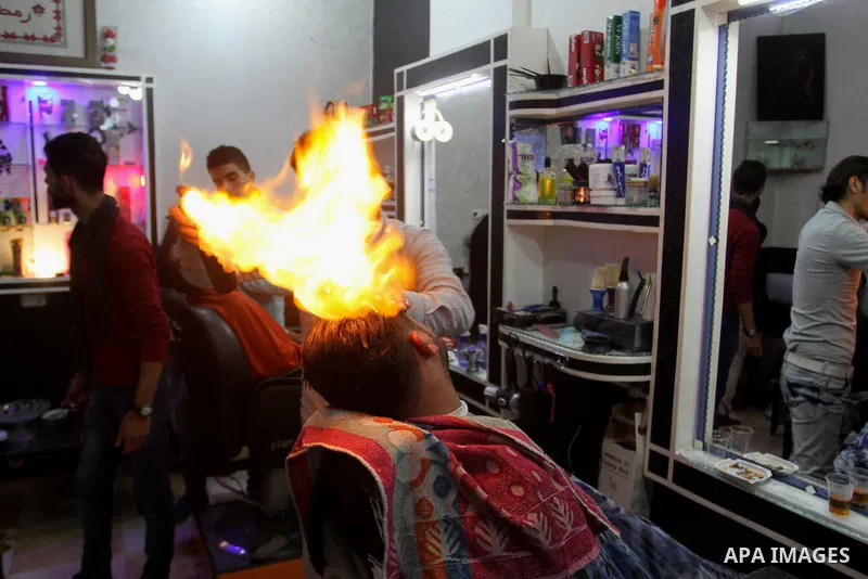 Ramadan Edwan, a Palestinian barber, uses fire in a hair-straightening technique with a client at his salon in the Rafah refugee camp, in the southern Gaza Strip on February 2, 2017. Photo by Abed Rahim Khatib