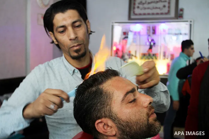 Ramadan Edwan, a Palestinian barber, uses fire in a hair-straightening technique with a client at his salon in the Rafah refugee camp, in the southern Gaza Strip on February 2, 2017. Photo by Abed Rahim Khatib
