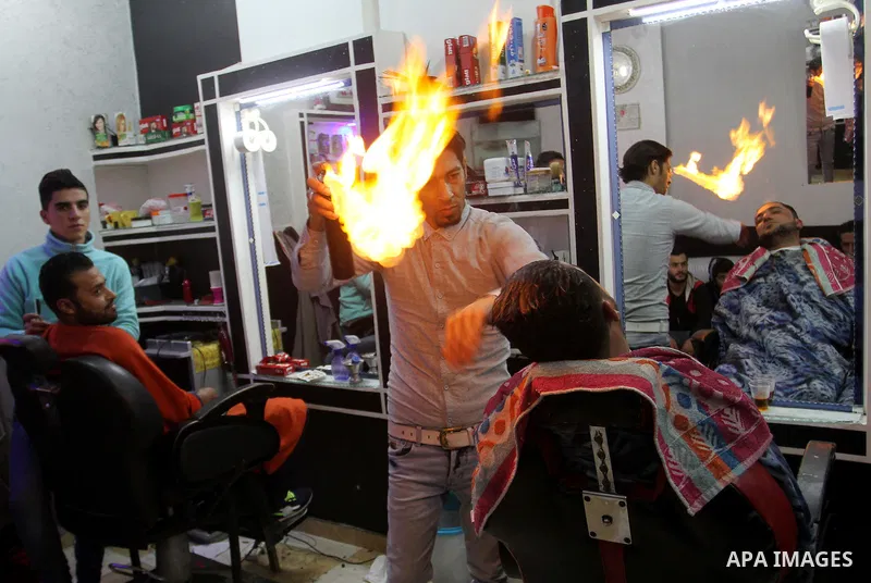 Ramadan Edwan, a Palestinian barber, uses fire in a hair-straightening technique with a client at his salon in the Rafah refugee camp, in the southern Gaza Strip on February 2, 2017. Photo by Abed Rahim Khatib