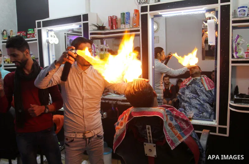 Ramadan Edwan, a Palestinian barber, uses fire in a hair-straightening technique with a client at his salon in the Rafah refugee camp, in the southern Gaza Strip on February 2, 2017. Photo by Abed Rahim Khatib