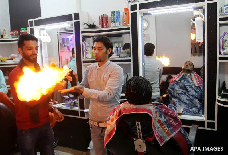 Ramadan Edwan, a Palestinian barber, uses fire in a hair-straightening technique with a client at his salon in the Rafah refugee camp, in the southern Gaza Strip on February 2, 2017. Photo by Abed Rahim Khatib